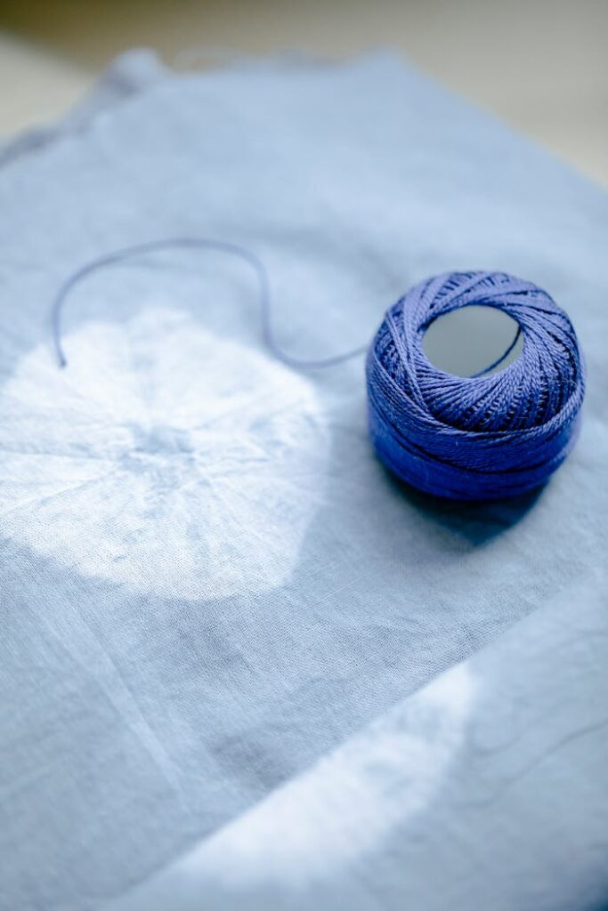 From above of blue yarn placed on fabric with creative round pattern in professional light studio using modern shibori dyeing technique